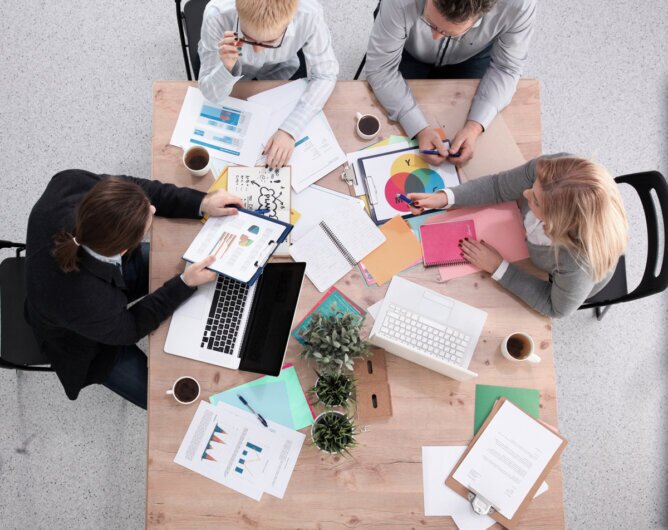 Das Photo zeigt vier Personen beim Arbeiten an einem Tisch mit vielen Papieren aus der Vogelperspektive.<br />©Stocknation