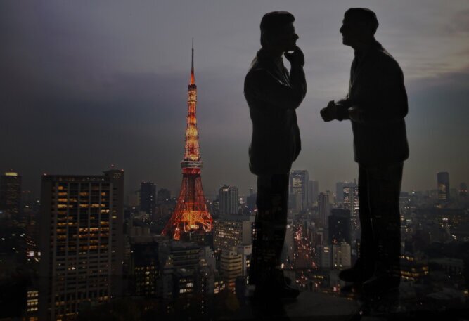 Das Photo zeigt zwei Mäner, die sich in einem Hochhaus vor der Skyline von Tokyo unterhalten..<br />©memephoto